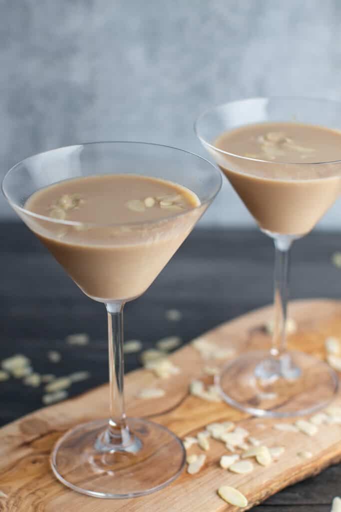 two glasses filled with dessert sitting on top of a wooden cutting board