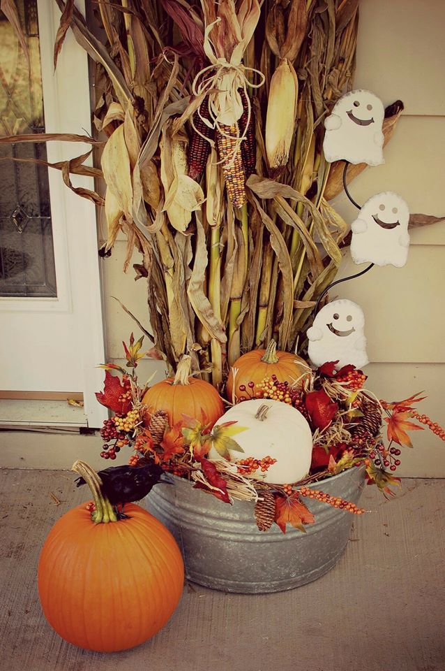 pumpkins and gourds are sitting on the front porch with fake corn stalks