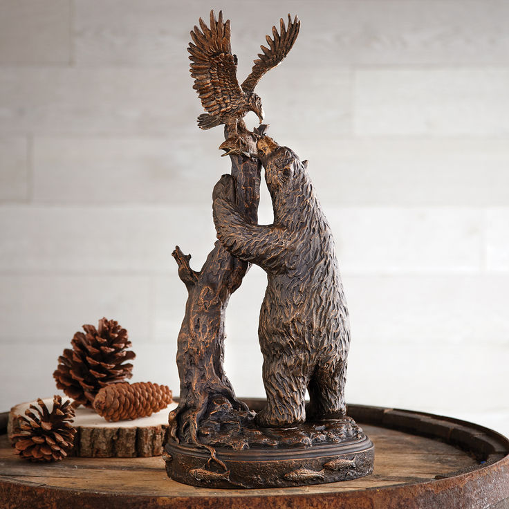 a bear and bird statue on top of a wooden table next to pinecones