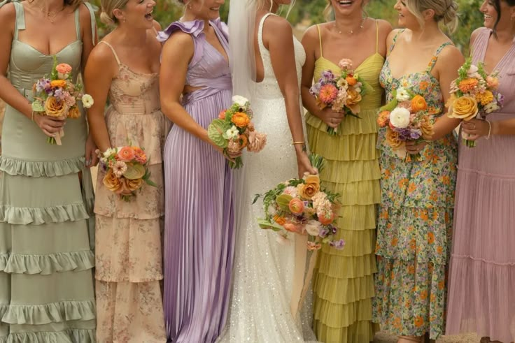 a group of women standing next to each other wearing dresses and holding bouquets in their hands