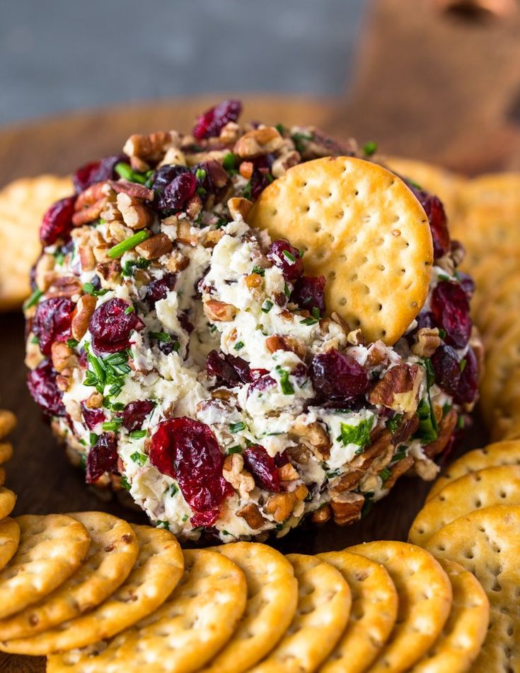 a cheese ball with crackers and cranberries on it sitting next to crackers