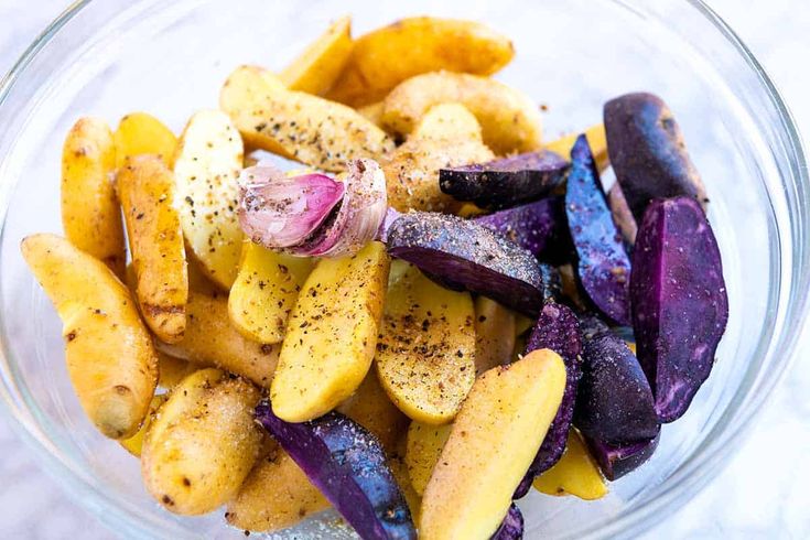 a glass bowl filled with sliced up purple and yellow veggies on top of a table