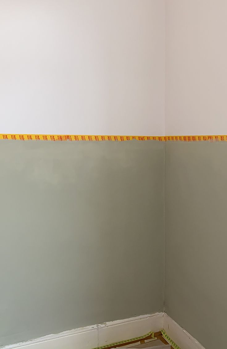 the corner of a room that is being painted in yellow and white with tape on it