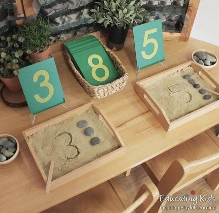 a wooden table topped with lots of sand covered in numbers and rocks next to potted plants