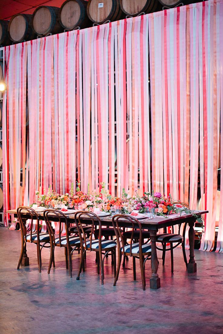 a long table is set up in front of some wine barrels with pink drapes