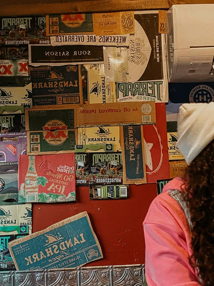 a woman standing in front of a red wall covered with posters and stickers on it