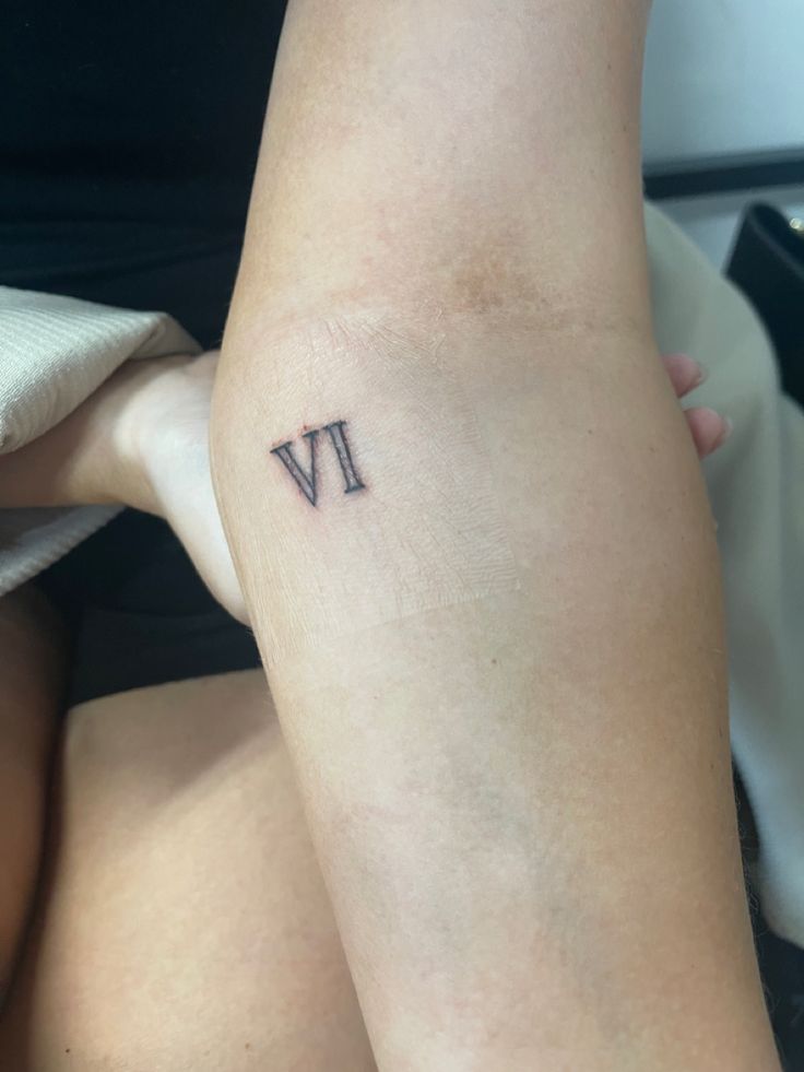 a person with a small tattoo on their arm that reads vv in roman numerals