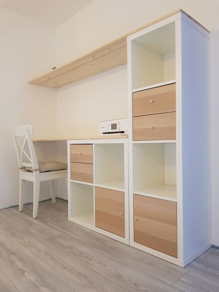 an empty room with white furniture and wooden shelves on the wall next to a chair