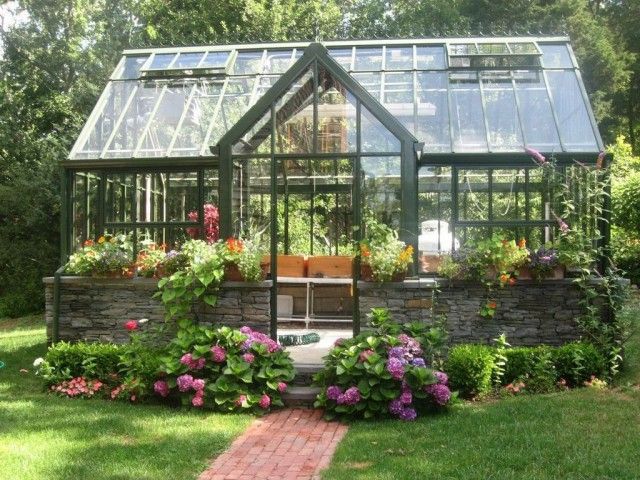 a small greenhouse in the middle of a garden with flowers and plants growing inside it