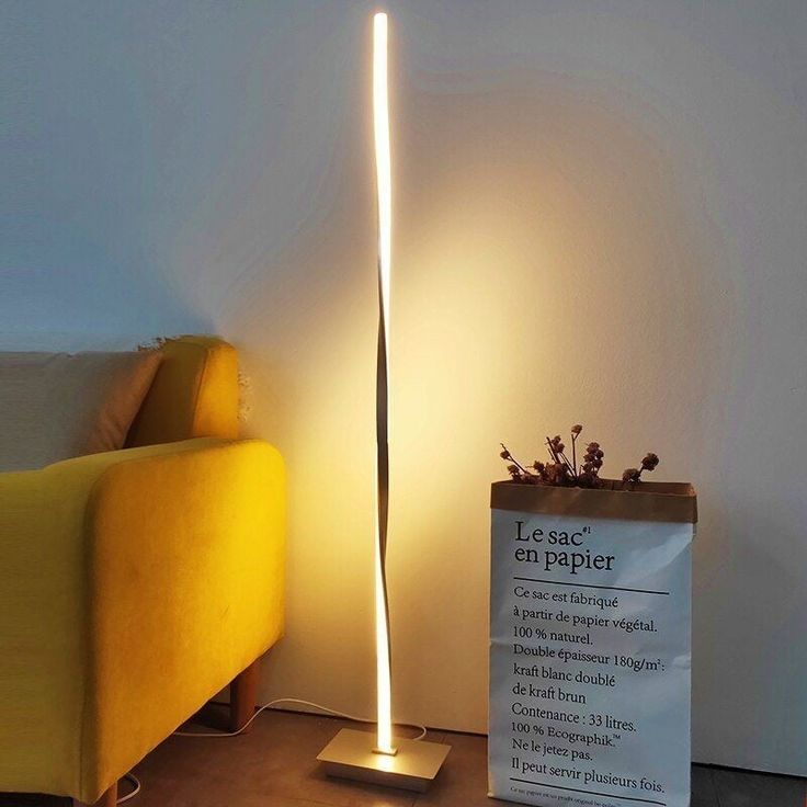 a yellow couch sitting next to a lamp on top of a wooden floor in front of a white wall