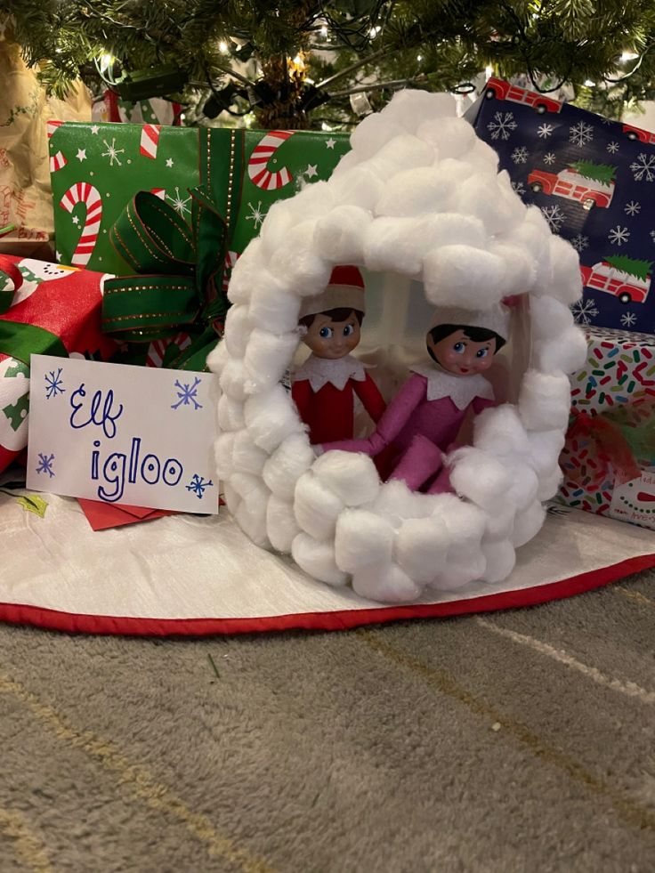 two elfs in a fake snowman's house surrounded by presents under a christmas tree