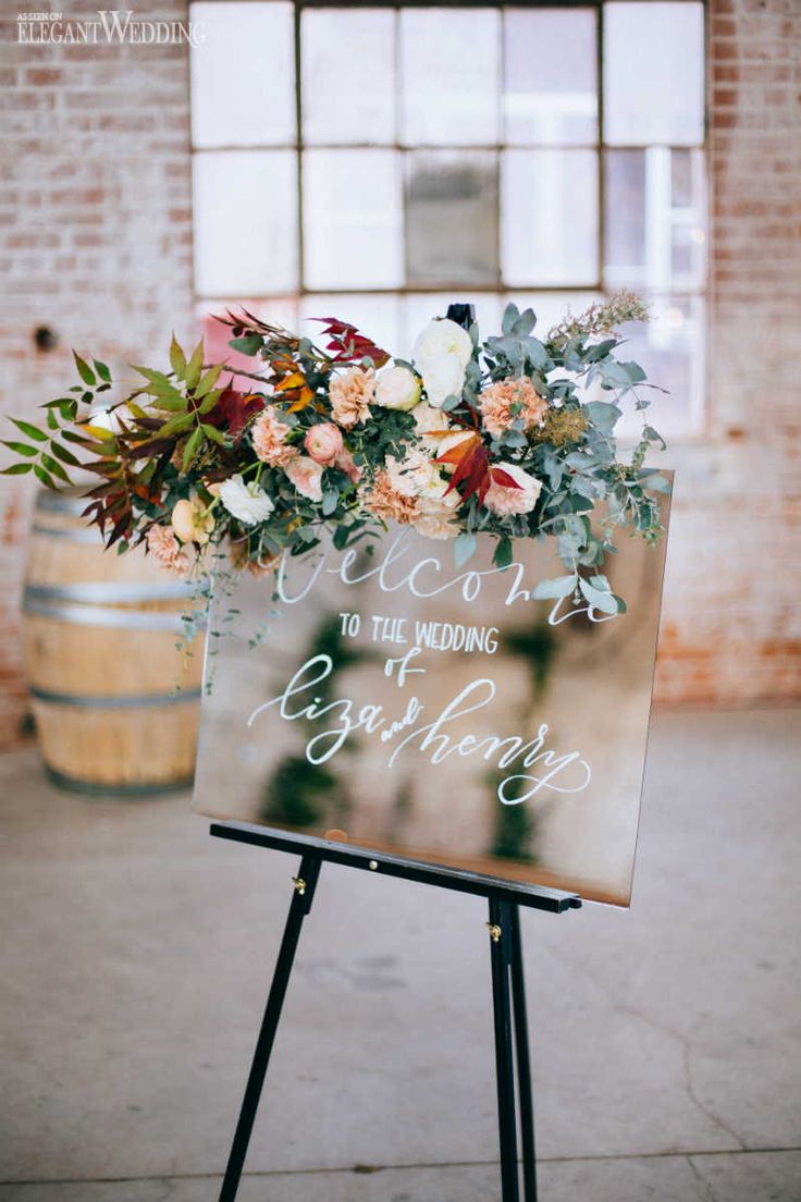 a welcome sign with flowers and greenery is displayed in front of a brick wall