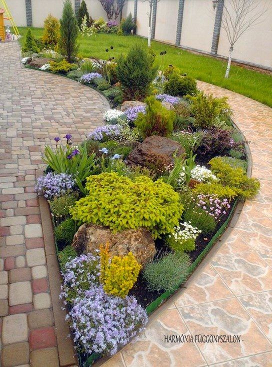 a garden with flowers and rocks in the middle on a brick walkway next to a fence