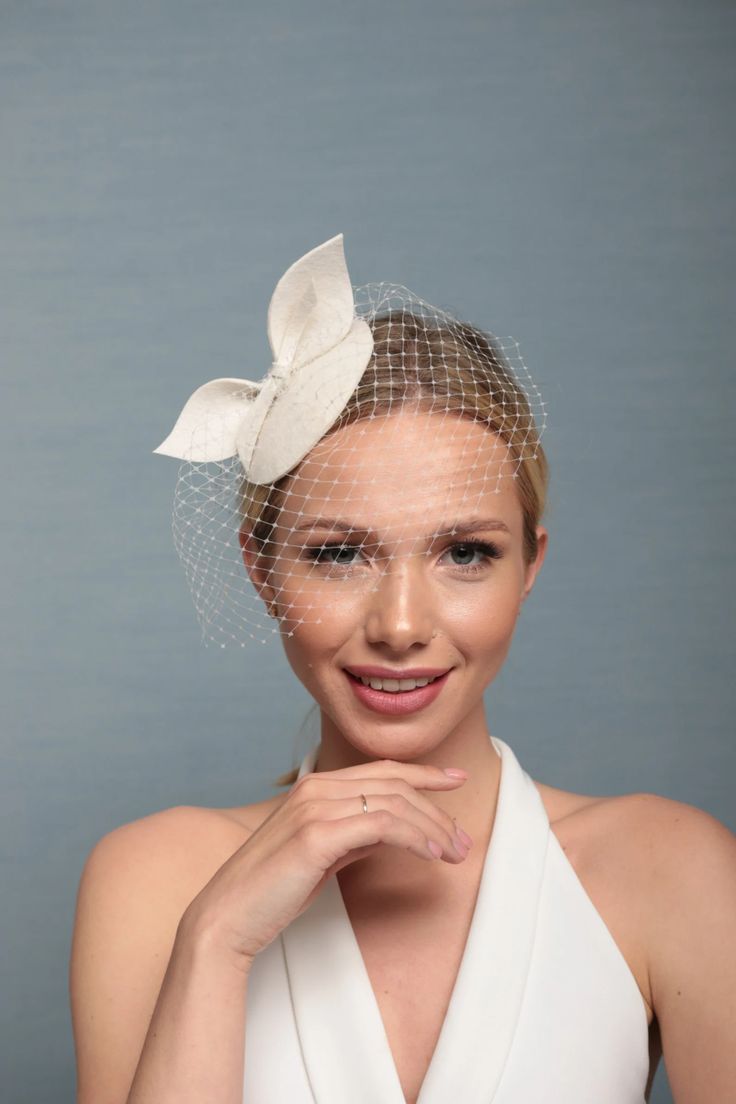 a woman wearing a veil with a white flower on it's head and holding her hand under her chin