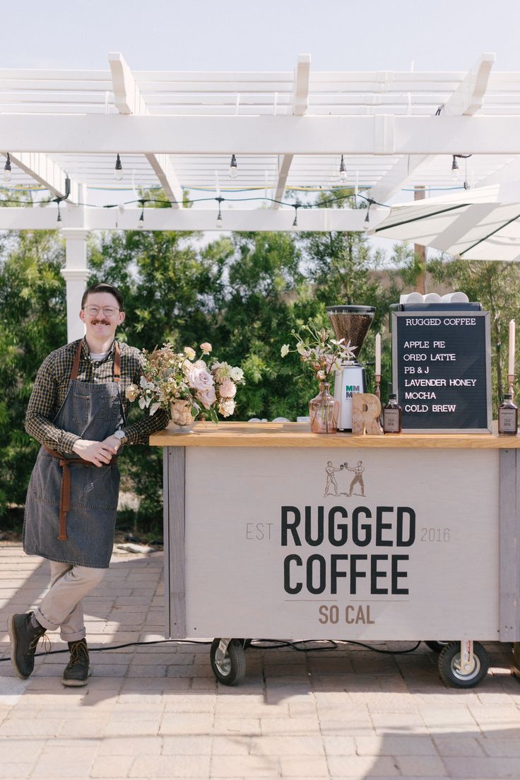 a man standing next to a coffee cart with flowers on the counter and a sign that says rugged coffee so call