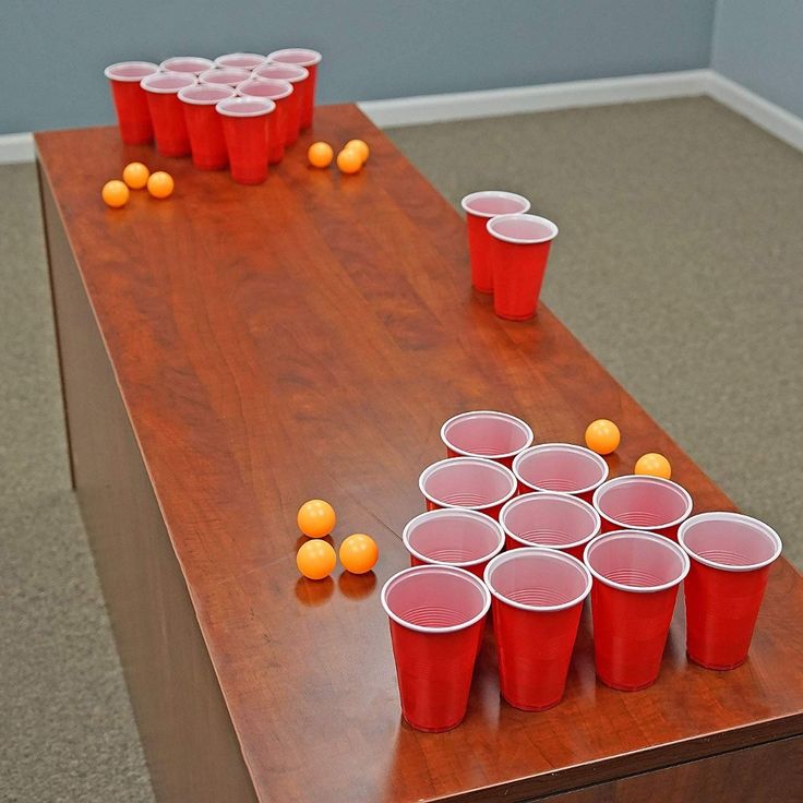 red cups are lined up on a table with orange balls scattered about it, and one cup has been placed in front of the other