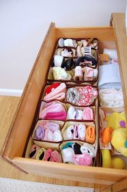 an open drawer filled with lots of baby items on top of a wooden floor next to a bed