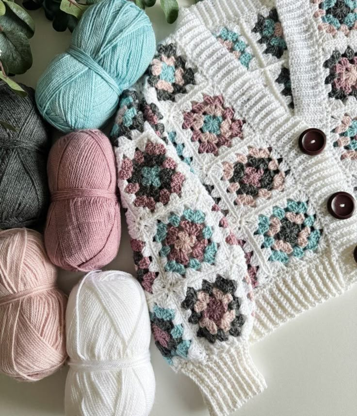 crocheted sweaters and balls of yarn are laid out next to each other