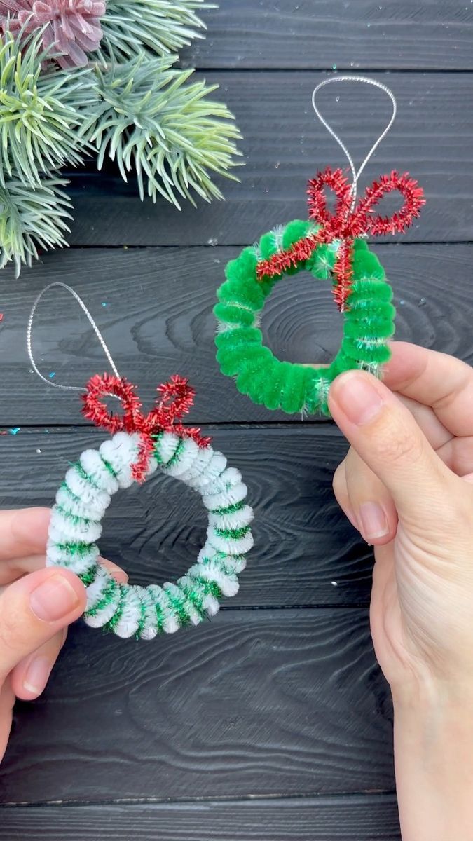 two handmade christmas wreath ornaments being held by someone's hands on a wooden table