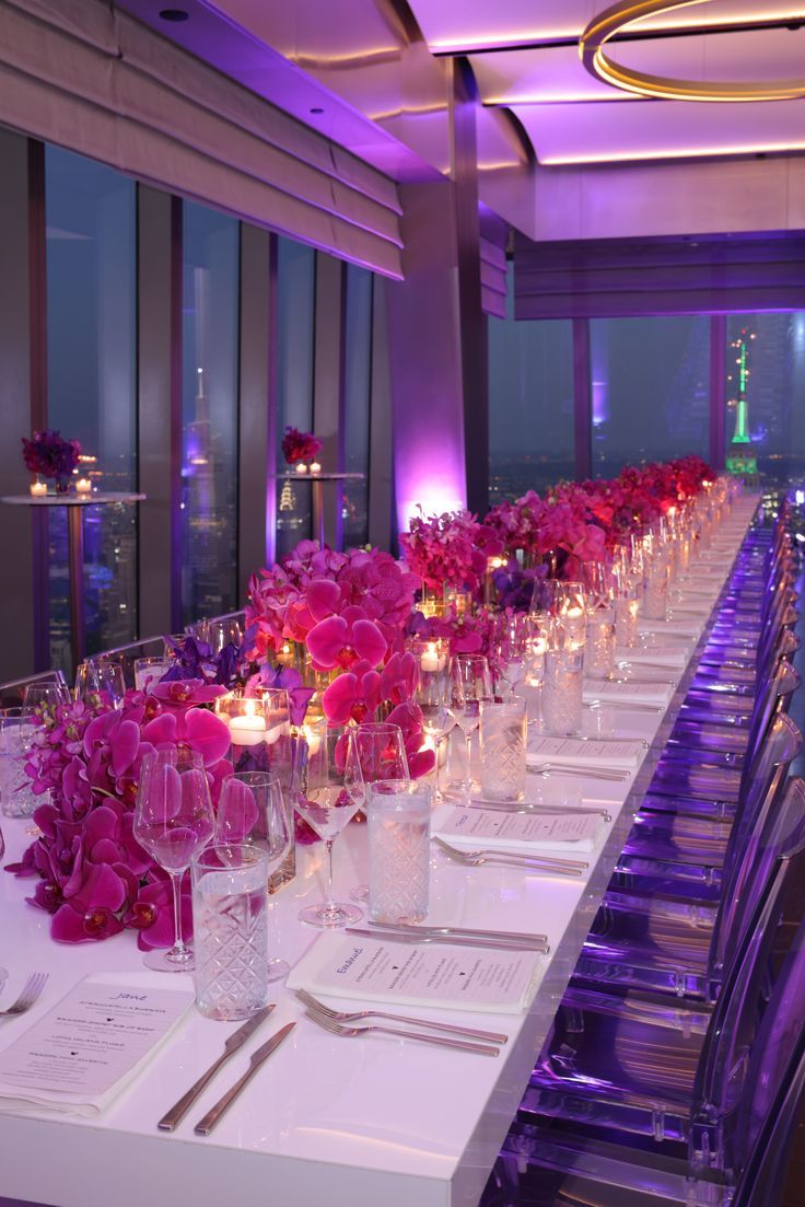 the long table is set with wine glasses and pink flowers on each side, along with candles