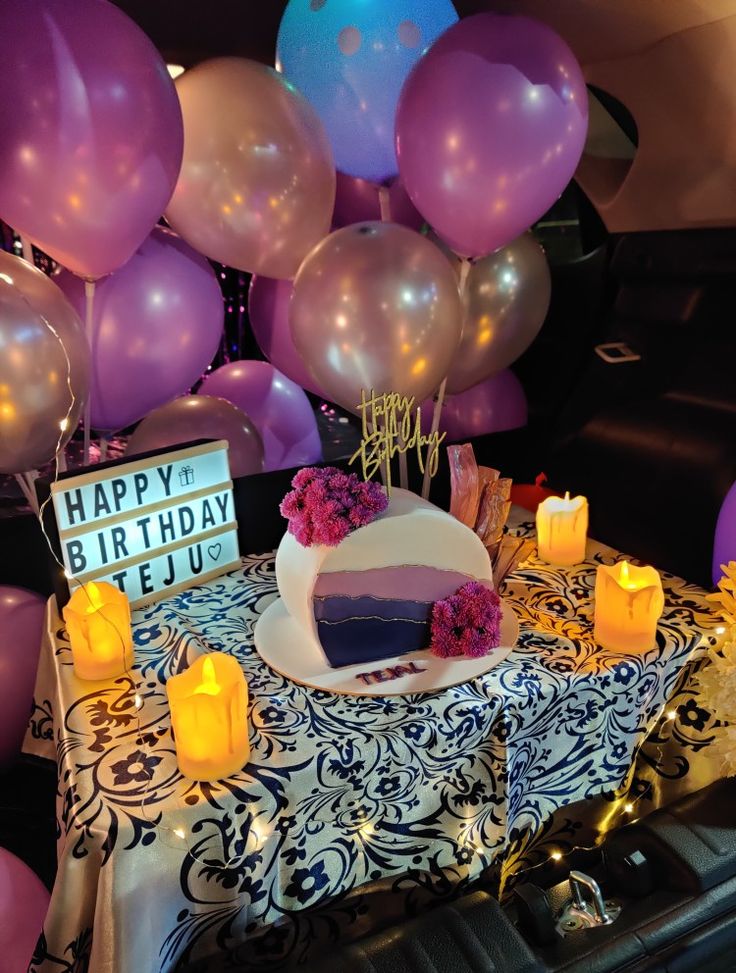 a birthday cake on a table with candles and balloons in the back seat of a car