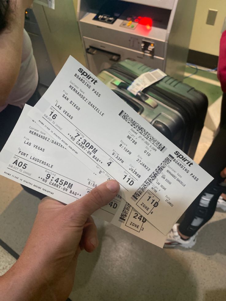 two tickets are being held up in front of an airport checkout counter with luggage