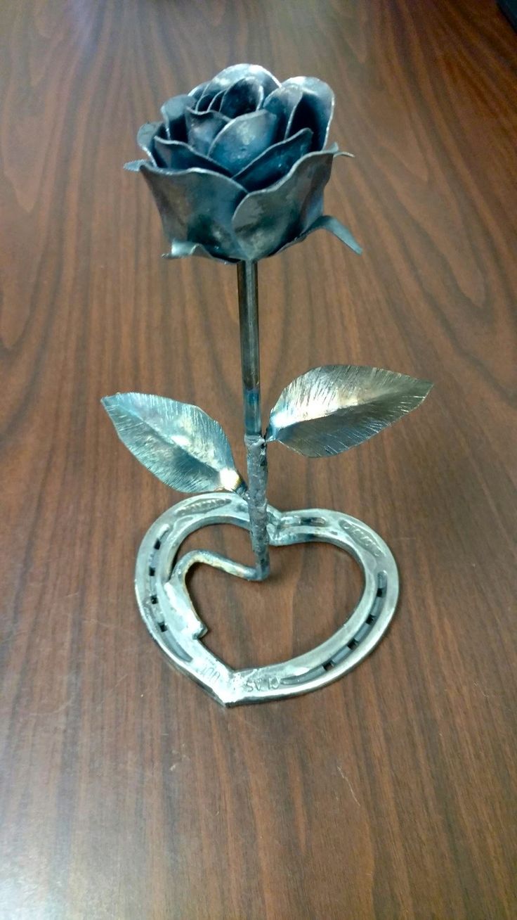 a metal rose sitting in the shape of a heart on top of a wooden table