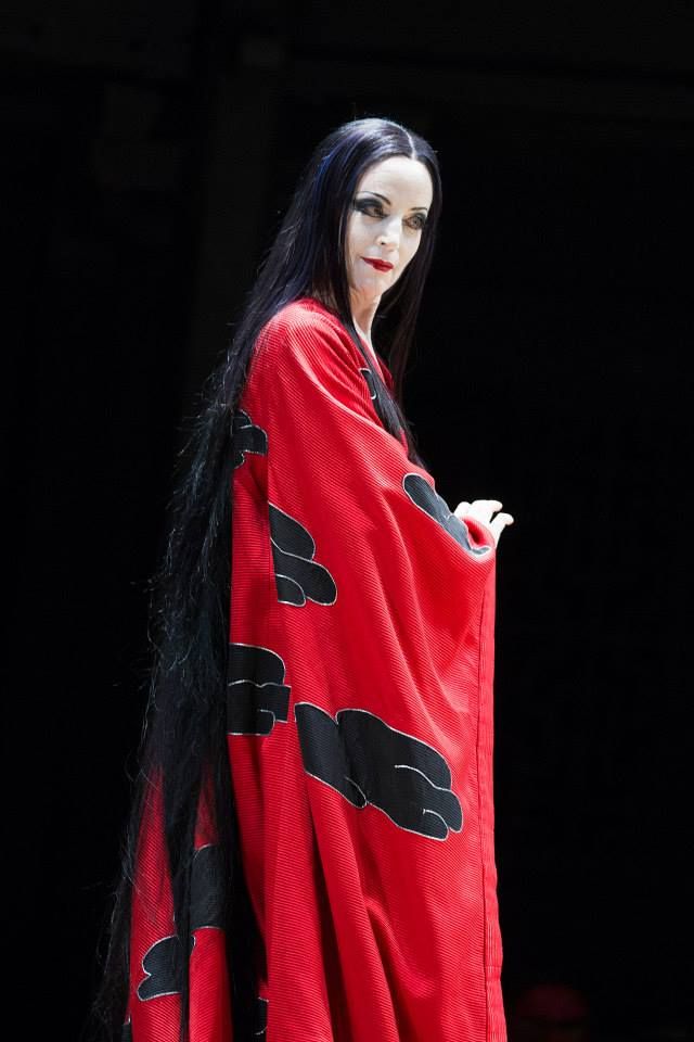 a woman with long black hair wearing a red cape and holding her hand on her hip