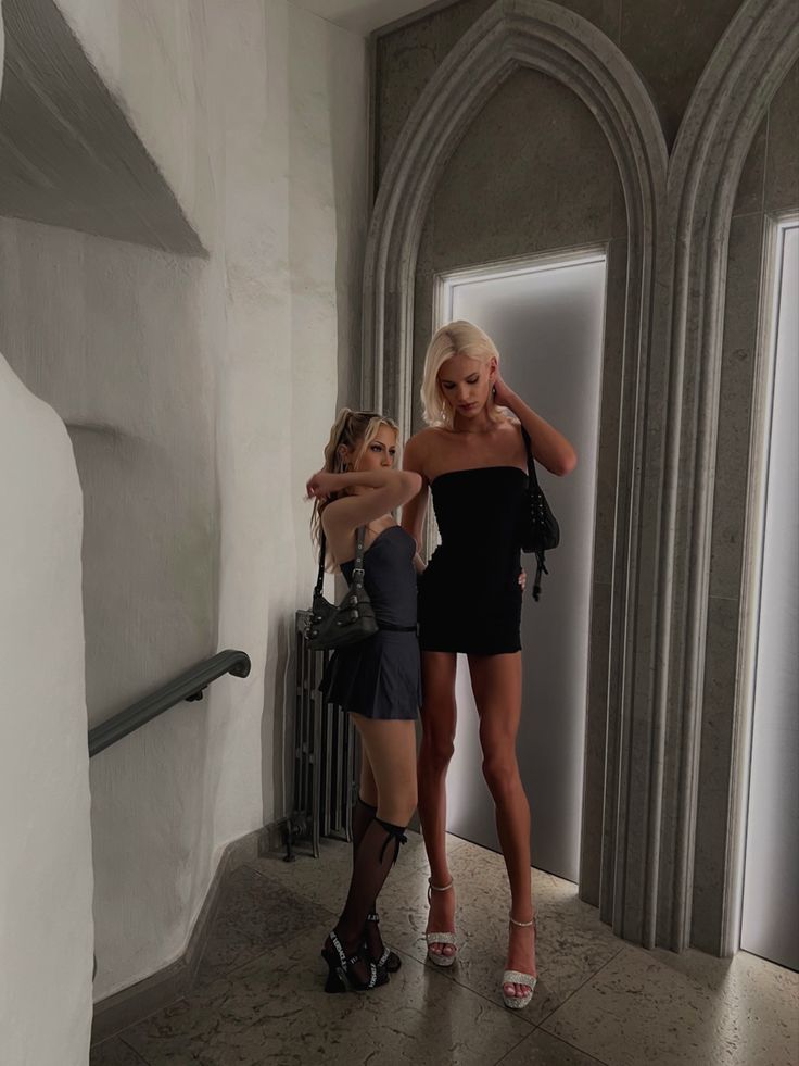 two beautiful women standing next to each other in front of a doorway with an open door