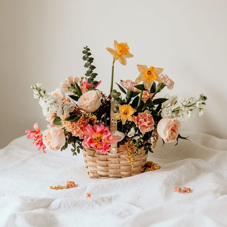 a basket filled with lots of flowers on top of a white bed covered in sheets