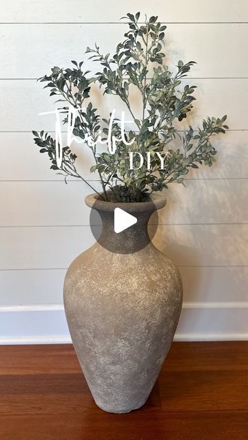 a vase with some plants in it on a wooden floor next to a white wall