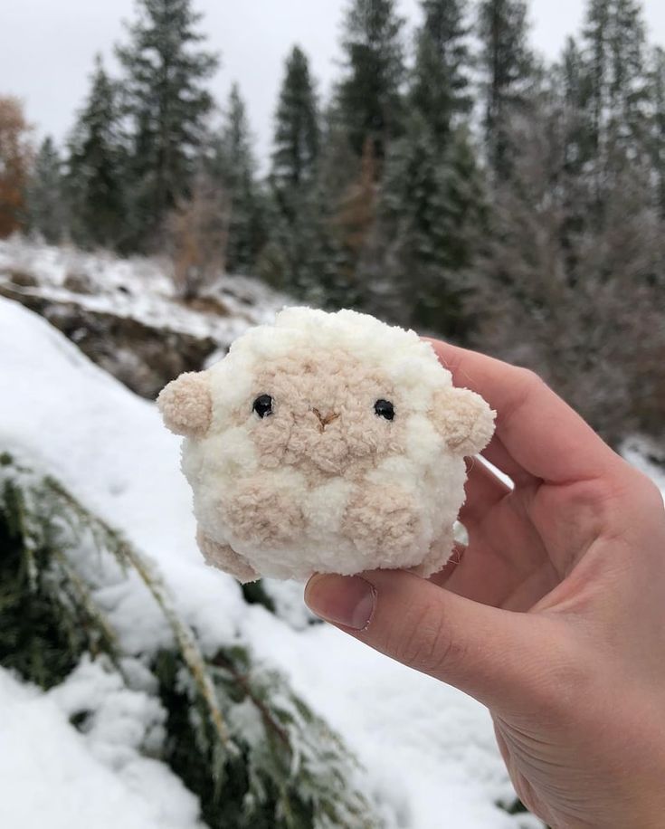 a hand holding a small stuffed animal in the snow