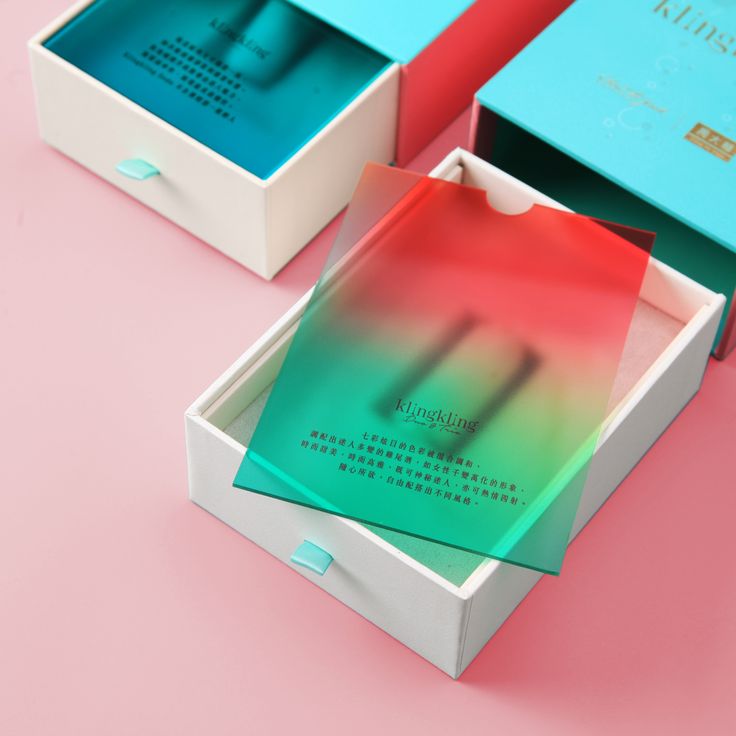 three boxes that are open on a pink surface with blue and green paper in them