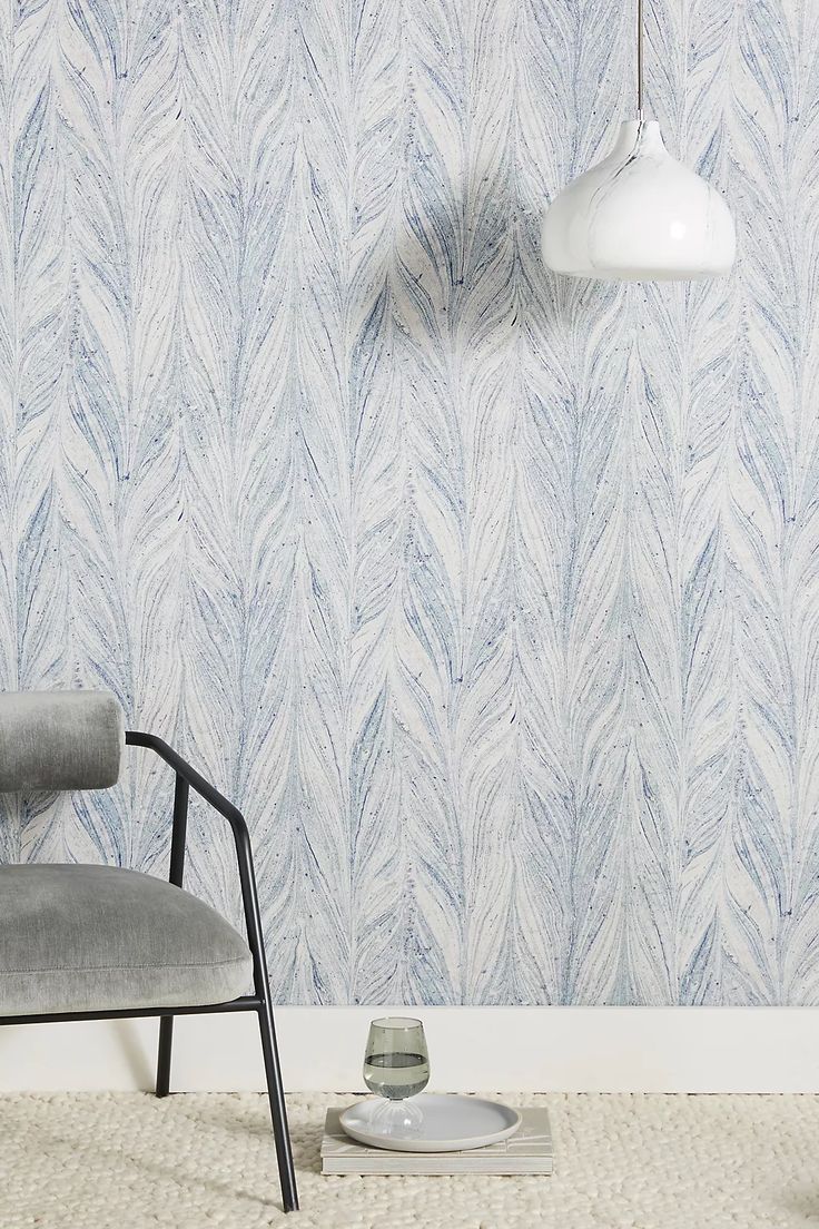 a gray chair sitting in front of a wall with a blue and white pattern on it