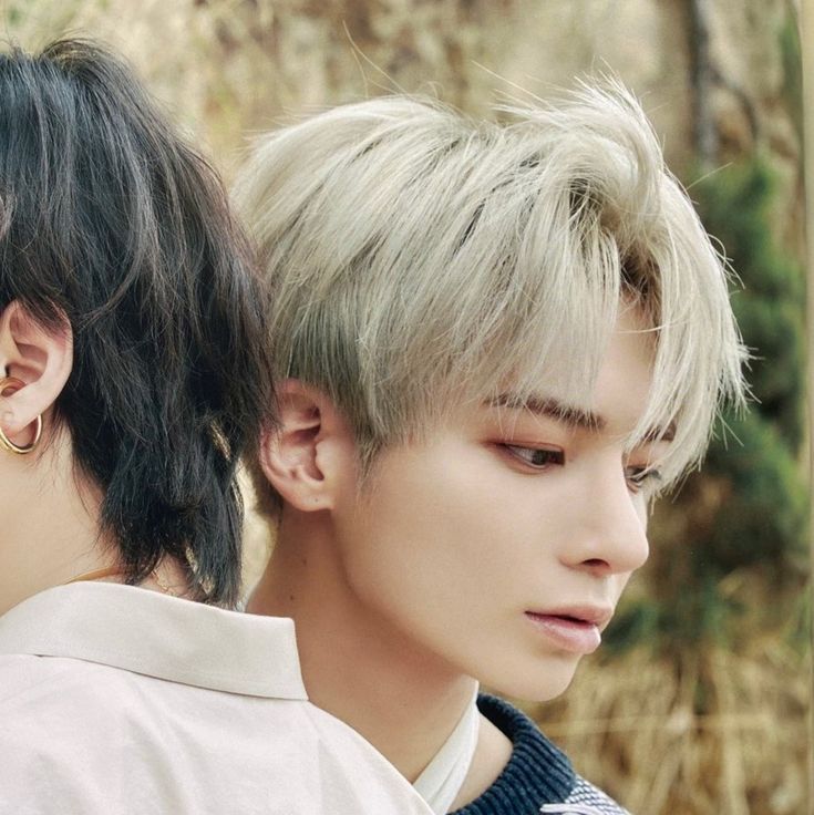 two young men standing next to each other in front of some trees and bushes with their eyes closed