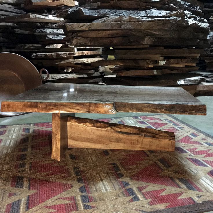 a wooden table sitting on top of a rug in front of stacks of wood planks