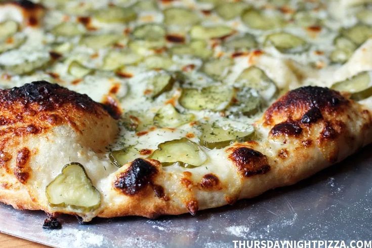 a close up of a pizza on a pan with cheese and pickle toppings