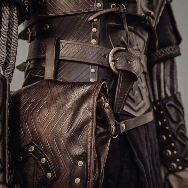 a close up of a person wearing leather armor and holding a brown bag with gold rivets