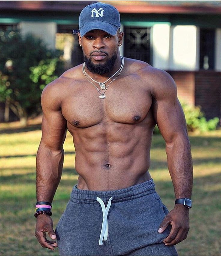 a shirtless man with no shirt on standing in front of a house wearing sweatpants and a baseball cap