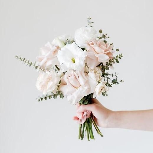 a bouquet of white and pink flowers being held by a person's hand against a white wall