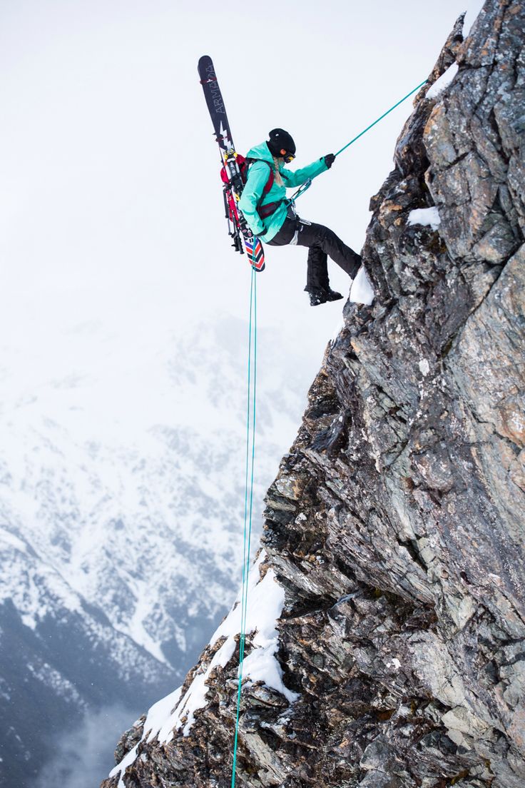 a man on skis hanging off the side of a mountain while holding onto a rope