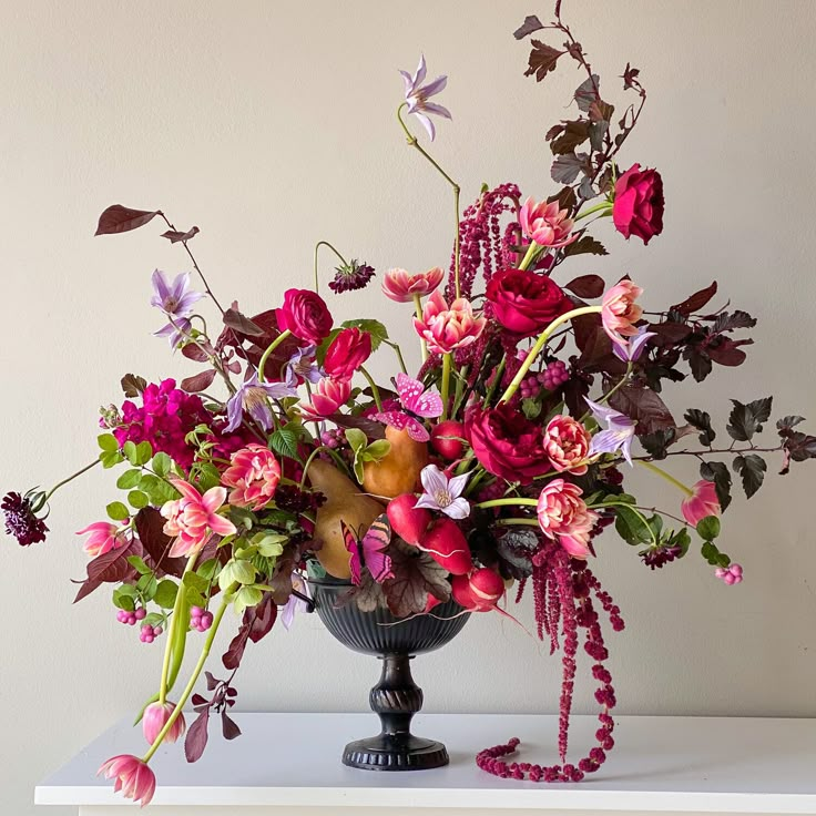 a vase filled with lots of colorful flowers on top of a white table next to a wall