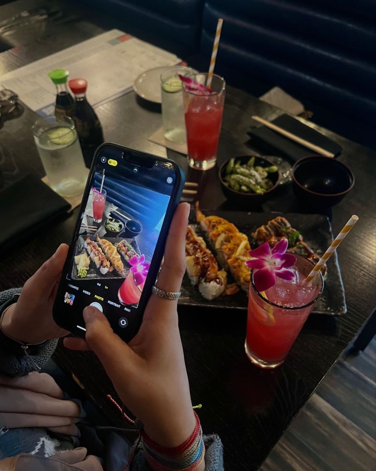 a person holding up a cell phone in front of food and drinks on a table