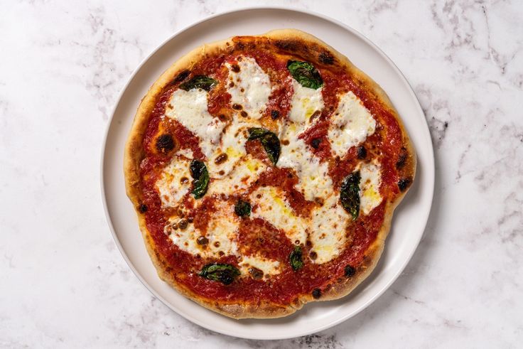 a pizza with cheese and spinach on a white plate sitting on a marble counter top