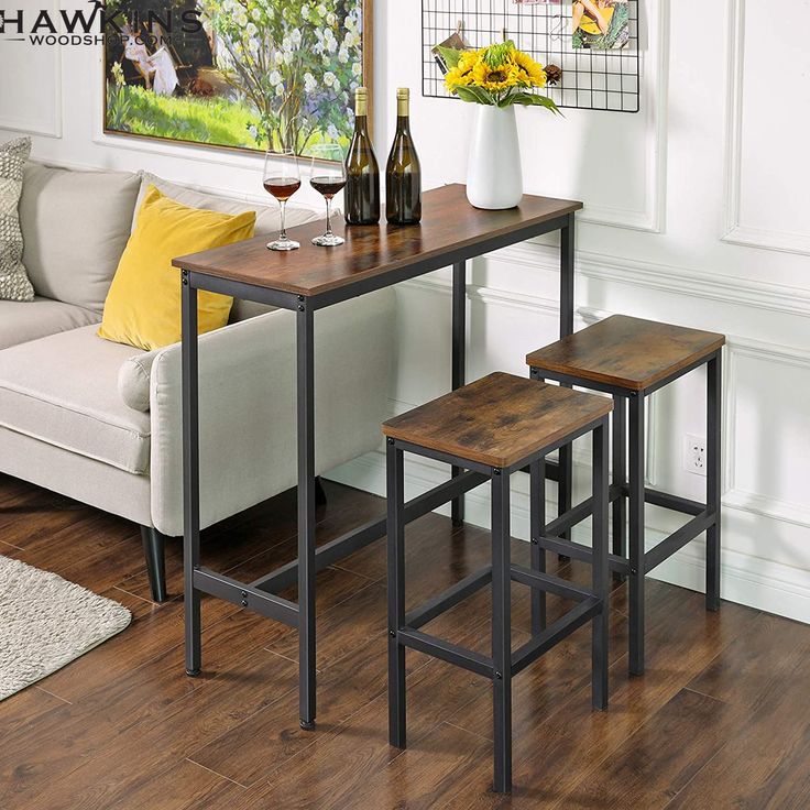 three stools and a table in a living room with white walls, wood flooring and artwork on the wall