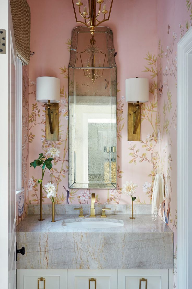 a bathroom with pink and gold wallpaper, marble counter top and vanity mirror above the sink