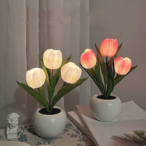 two white vases filled with pink flowers on top of a table next to an open book