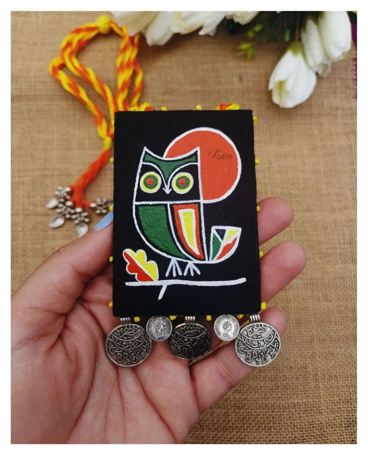 a hand holding a small card with an owl on it's back and three coins in front of it