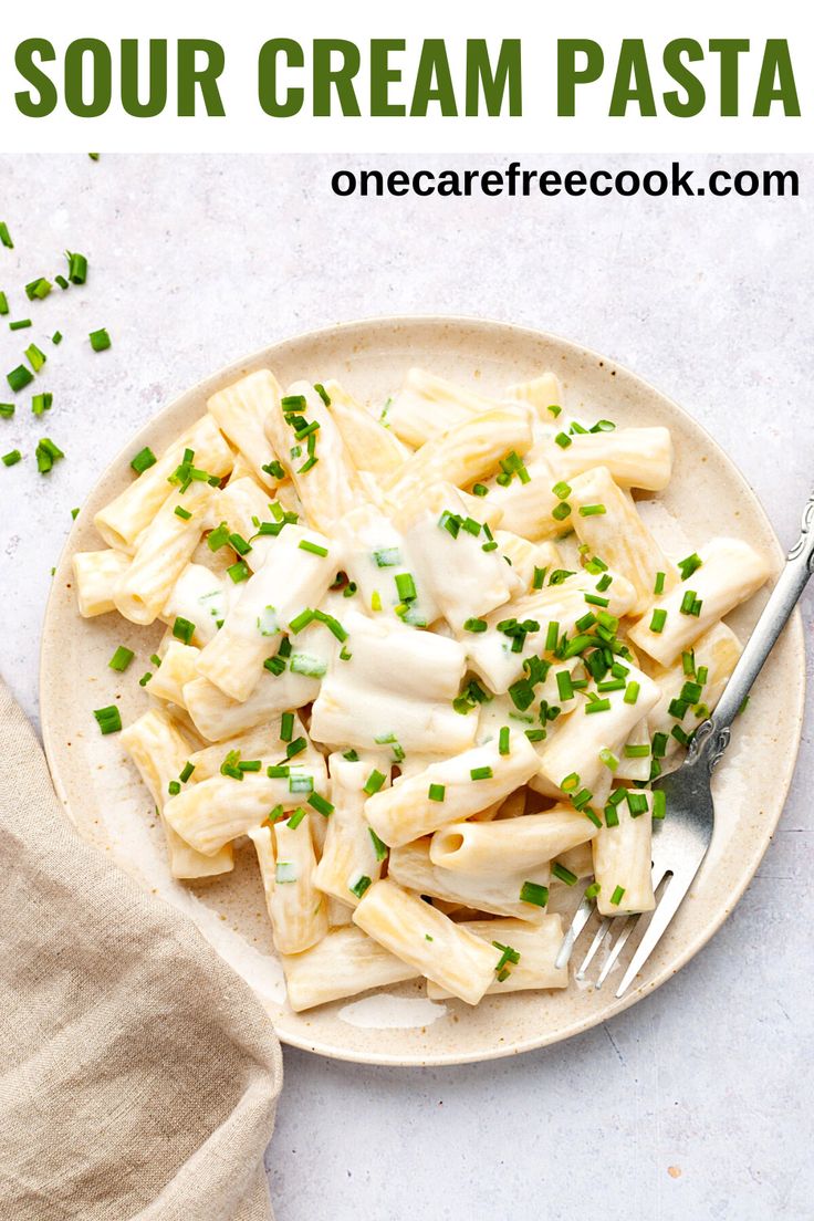 a white plate topped with pasta covered in cheese and chives next to a fork