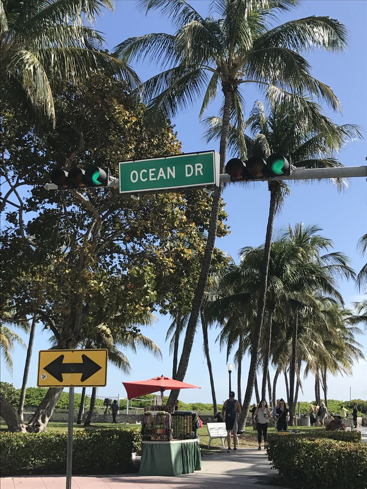 a street sign that reads ocean dr with palm trees in the back ground and people walking on the sidewalk